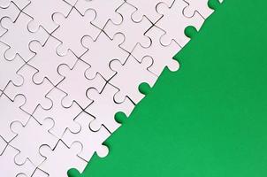 Fragment of a folded white jigsaw puzzle on the background of a green plastic surface. Texture photo with copy space for text