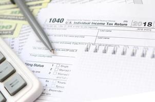 The pen, notebook, calculator, and dollar bills is lies on the tax form 1040 U.S. Individual Income Tax Return. The time to pay taxes photo