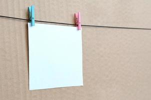 White blank card on rope on a brown cardboard background. Creative reminder, small sheet of paper on wooden clothespin, memo backdrop photo