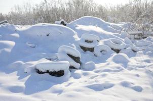 los neumáticos de automóviles usados y desechados yacen al costado de la carretera, cubiertos con una gruesa capa de nieve foto