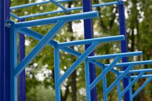 tubos de metal azul y barras transversales contra un campo de deportes callejeros para entrenar en atletismo. equipo de gimnasia atlética al aire libre. foto macro con enfoque selectivo y fondo extremadamente borroso