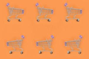 Shopping addiction, shopping lover or shopaholic concept. Many small empty shopping carts perform a pattern on a pastel colored paper background. Flat lay composition, top view photo