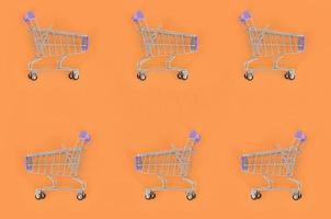 Shopping addiction, shopping lover or shopaholic concept. Many small empty shopping carts perform a pattern on a pastel colored paper background. Flat lay composition, top view photo