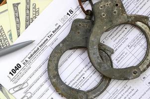 Police handcuffs lie on the tax form 1040. The concept of problems with the law in the aftermath of non-payment of taxes photo