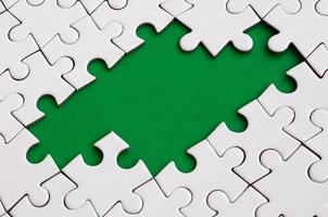 Close-up texture of a white jigsaw puzzle in assembled state with missing elements forming a green pad for text. Copy space photo