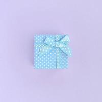Small blue gift box with ribbon lies on a violet background. Minimalism flat lay top view photo