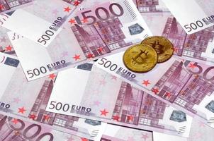 Bitcoins over pile of five hundred euro banknotes. Traditional money versus cryptocurrency concept. Gold coin above 500 euro bills. Close up photo