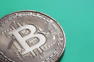 Chocolate product in the form of physical bitcoin lies on a green plastic background. Model of the crypto currency in the edible form photo