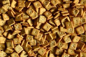 A lot of small cookies are square shaped. A pattern of a yellow salt cracker. Background image with salted pastry photo