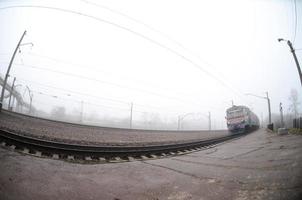 The Ukrainian suburban train rushes along the railway in a misty morning. Fisheye photo with increased distortion