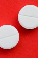 A few white tablets lie on a bright red background surface. Background image on medical and pharmaceutical topics photo