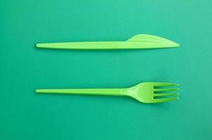 Disposable plastic cutlery green. Plastic fork and knife lie on a green background surface photo