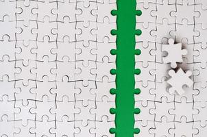 The green path is laid on the platform of a white folded jigsaw puzzle. The missing elements of the puzzle are stacked nearby. Texture image with space for text photo