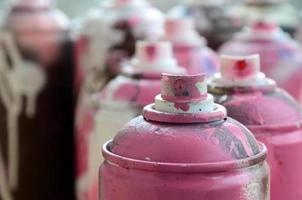 A lot of dirty and used aerosol cans of bright pink paint. Macro photograph with shallow depth of field. Selective focus on the spray nozzle photo