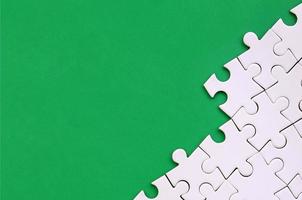 Fragment of a folded white jigsaw puzzle on the background of a green plastic surface. Texture photo with copy space for text