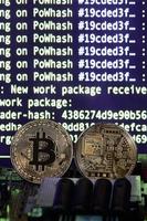 Two bitcoins lies on a videocard surface with background of screen display of cryptocurrency mining by using the GPUs photo