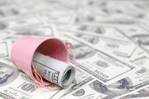 A bundle of US dollars in a metal pink bucket on a set of dollar bills photo