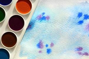 A new set of watercolors lies on a sheet of paper, which shows an abstract watercolor drawing in the form of blue strokes. The concept of amateur painting among teenagers photo