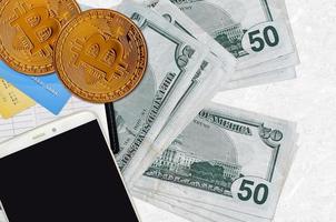 Billetes de 50 dólares estadounidenses y bitcoins dorados con smartphone y tarjetas de crédito. concepto de inversión en criptomonedas. criptominería o comercio foto