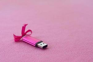 la tarjeta de memoria flash usb de color rosa brillante con un lazo rosa yace sobre una manta de suave y peluda tela de vellón rosa claro. diseño clásico de regalo femenino para una tarjeta de memoria foto