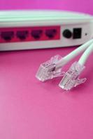 el enrutador de Internet y los enchufes del cable de Internet se encuentran sobre un fondo rosa brillante. elementos necesarios para internet foto