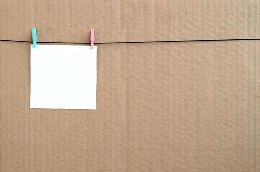 White blank card on rope on a brown cardboard background. Creative reminder, small sheet of paper on wooden clothespin, memo backdrop photo