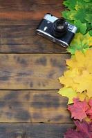 The old camera among a set of yellowing fallen autumn leaves on a background surface of natural wooden boards of dark brown color photo