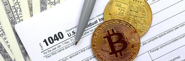 The pen, bitcoins and dollar bills is lies on the tax form 1040 U.S. Individual Income Tax Return. The time to pay taxes photo