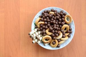 túbulos crujientes, bolas de fusión de chocolate y bagels yacen en un plato blanco sobre una mesa de madera. mezcla de varios dulces foto