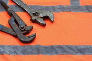 Adjustable and pipe wrenches against the background of an orange signal worker shirt photo