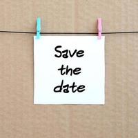 Save the date. Note is written on a white sticker that hangs with a clothespin on a rope on a background of brown cardboard photo