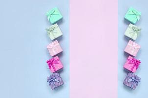 Small gift boxes of different colors with ribbons lies on a violet and pink background photo