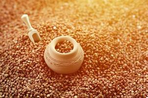 Background image of a large pile of buckwheat, in the middle of which lies a small jug and a wooden spatula for cereals photo