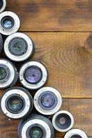 Several photographic lenses lie on a brown wooden background. Space for text photo