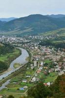 A beautiful view of the village of Mezhgorye, Carpathian region. A lot of residential buildings surrounded by high forest mountains and long river photo