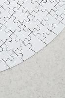A white jigsaw puzzle in the complete form lies on a treated stone surface. Textured image with copy space photo