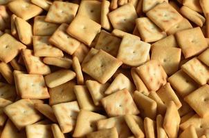 A lot of small cookies are square shaped. A pattern of a yellow salt cracker. Background image with salted pastry photo