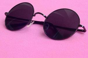 Stylish black sunglasses with round glasses lies on a blanket made of soft and fluffy light pink fleece fabric. Fashionable background picture in female colors photo