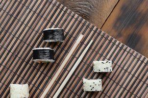 los rollos de sushi y los palillos de madera yacen sobre una alfombra de paja de bambú. comida asiática tradicional. vista superior foto
