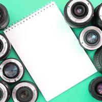 varias lentes fotográficas y un cuaderno blanco yacen sobre un fondo turquesa brillante. copie el espacio foto