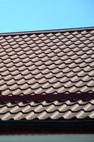 A fragment of a roof from a metal tile of dark red color. Quality Roofing photo