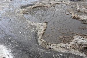 Damaged asphalt road with potholes caused by freezing and thawing cycles during the winter. Poor road photo