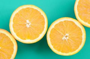Top view of a several orange fruit slices on bright background in turquoise green color. A saturated citrus texture image photo
