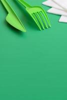 Disposable plastic cutlery green. Plastic fork and knife lie on a green background surface next to napkins photo