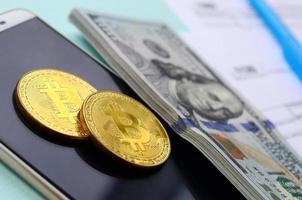 bitcoins se encuentra con los formularios de impuestos, los billetes de cien dólares y el teléfono inteligente en un fondo azul claro. declaración de la renta foto