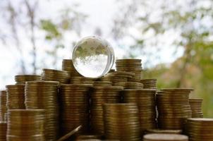 Glass planet on big pile of shiny ukrainian old 1 hryvnia coin stacks close up on blurred green trees background. The concept of money transfer around whole world photo