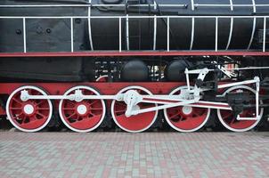 ruedas de la vieja locomotora de vapor negra de la época soviética. el lado de la locomotora con elementos de la tecnología giratoria de trenes antiguos foto