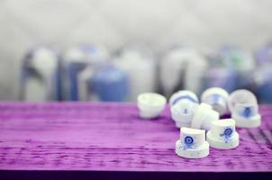 The soiled blue nozzles from the paint sprayer lies on a purple plank on a background of a many dirty spray cans photo