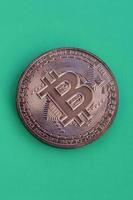 Chocolate product in the form of physical bitcoin lies on a green plastic background. Model of the crypto currency in the edible form photo