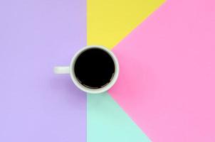 Small white coffee cup on texture background of fashion pastel blue, yellow, violet and pink colors paper in minimal concept photo